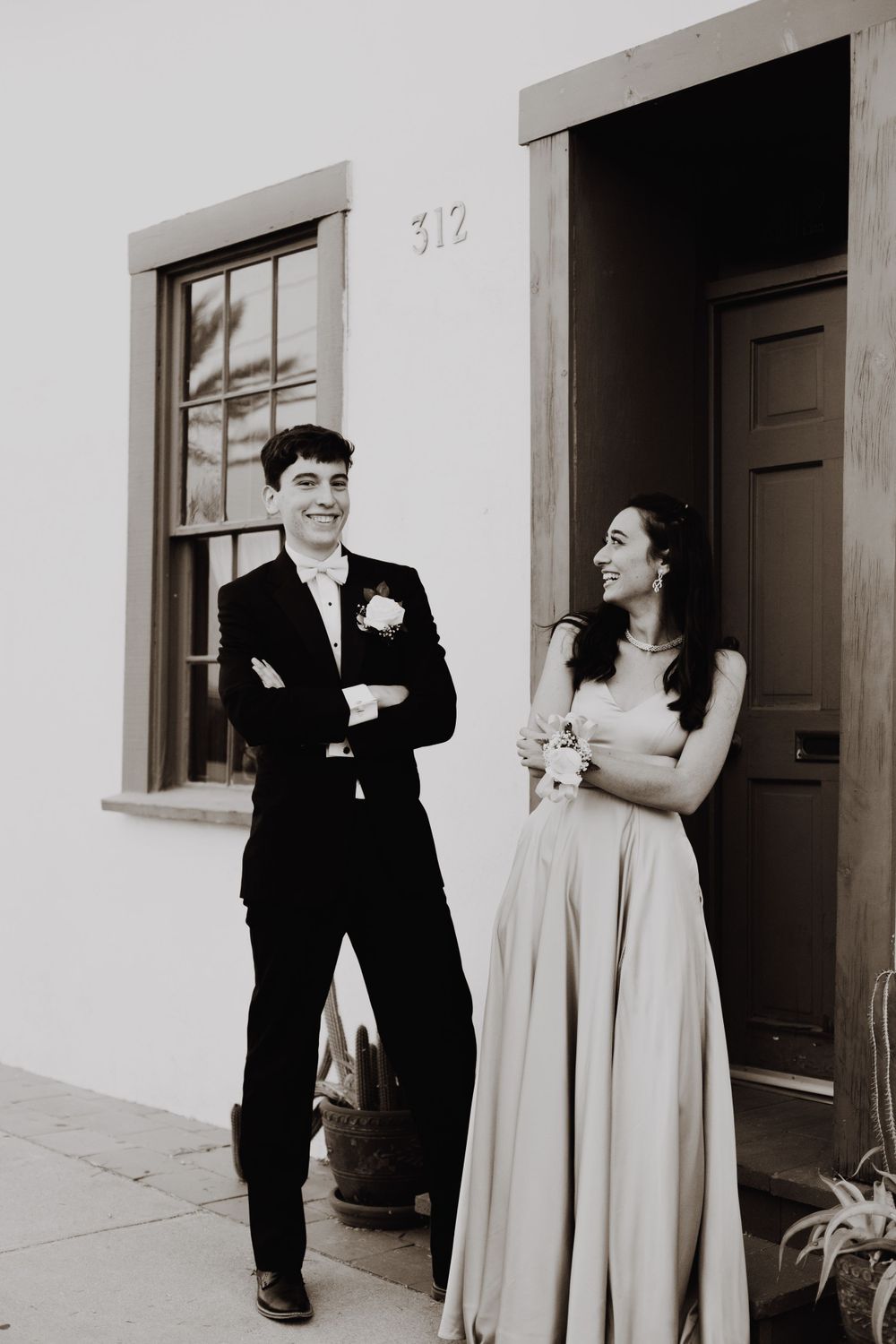 A couple in formal attire shares a candid moment outside a white building with address number 312.