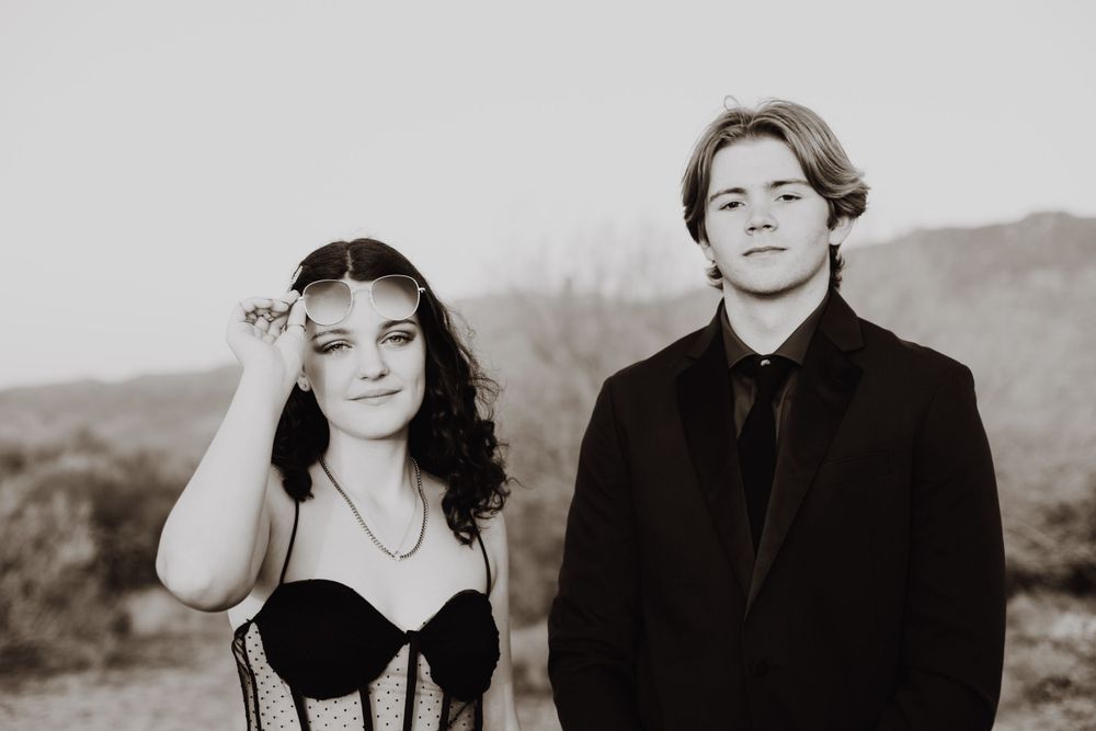 A black and white portrait of two people in formal wear against a mountain backdrop.