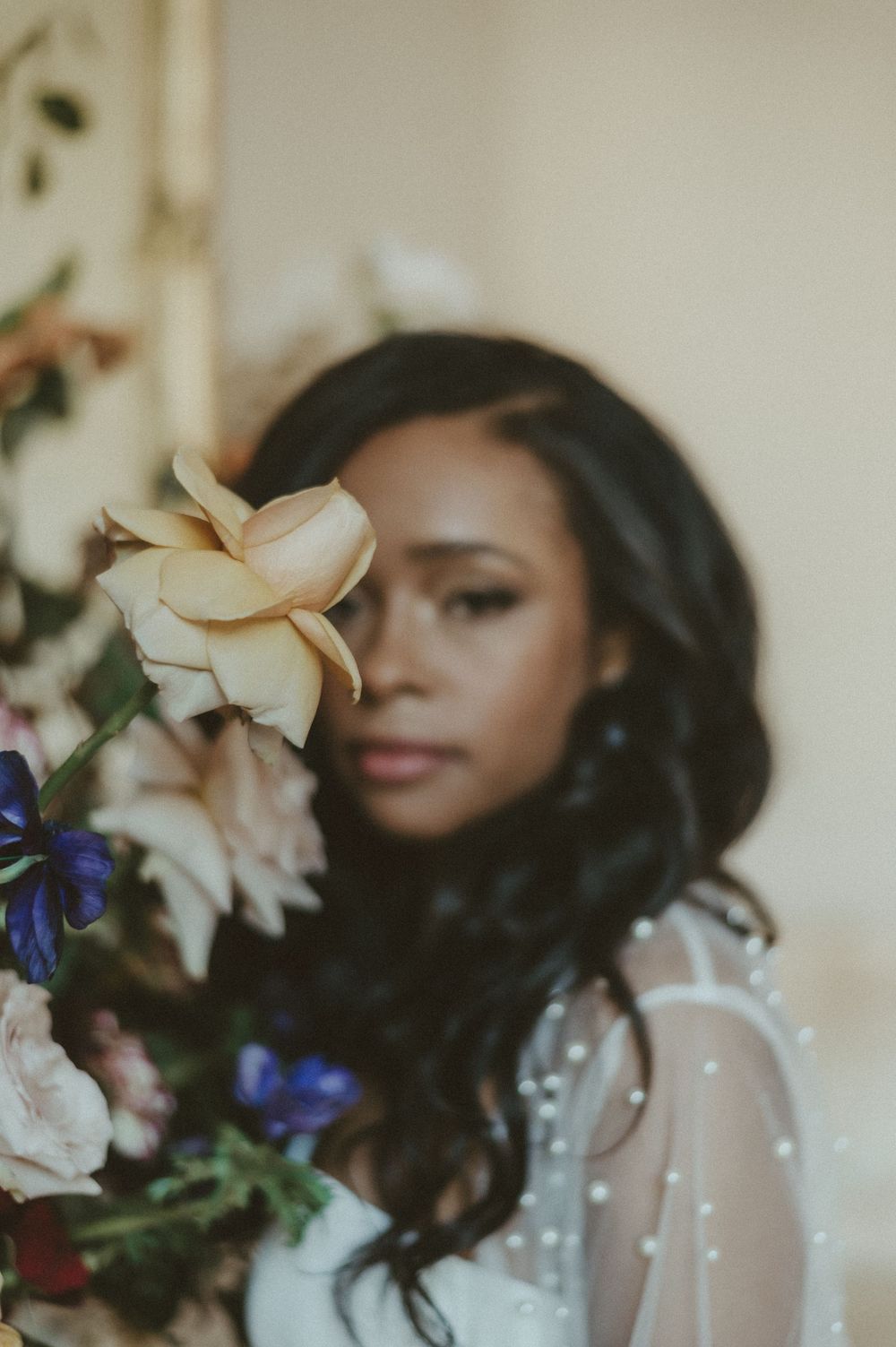 Artistic bridal photo with delicate flowers and sheer pearl-embellished wedding gown.