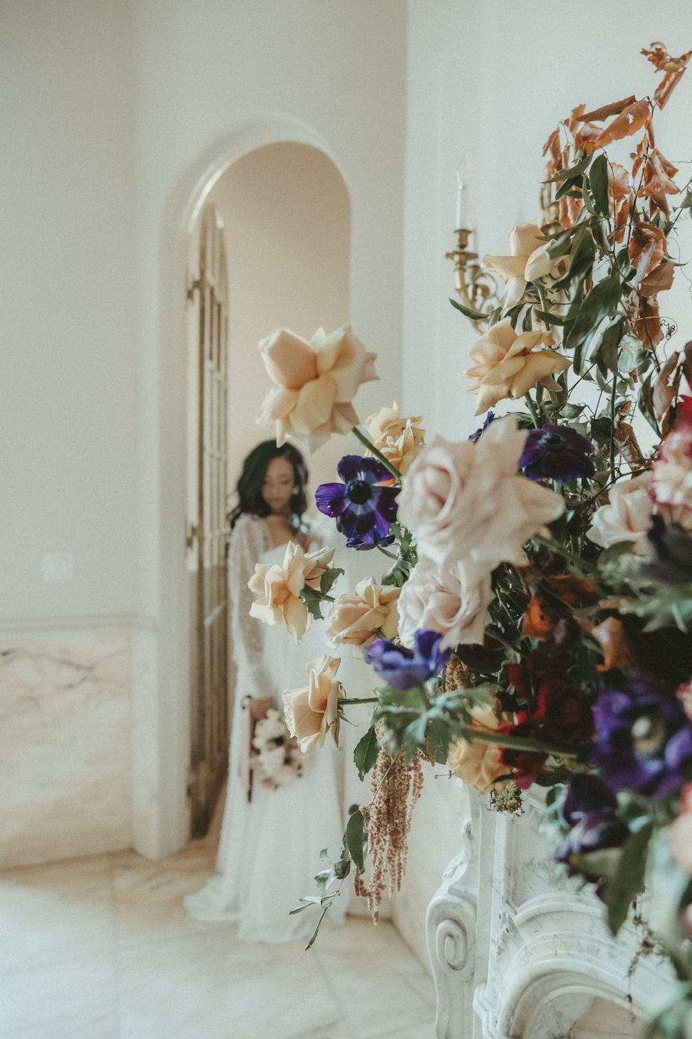 Elegant floral arrangement with peach and purple blooms decorates a white interior space with arched doorway.