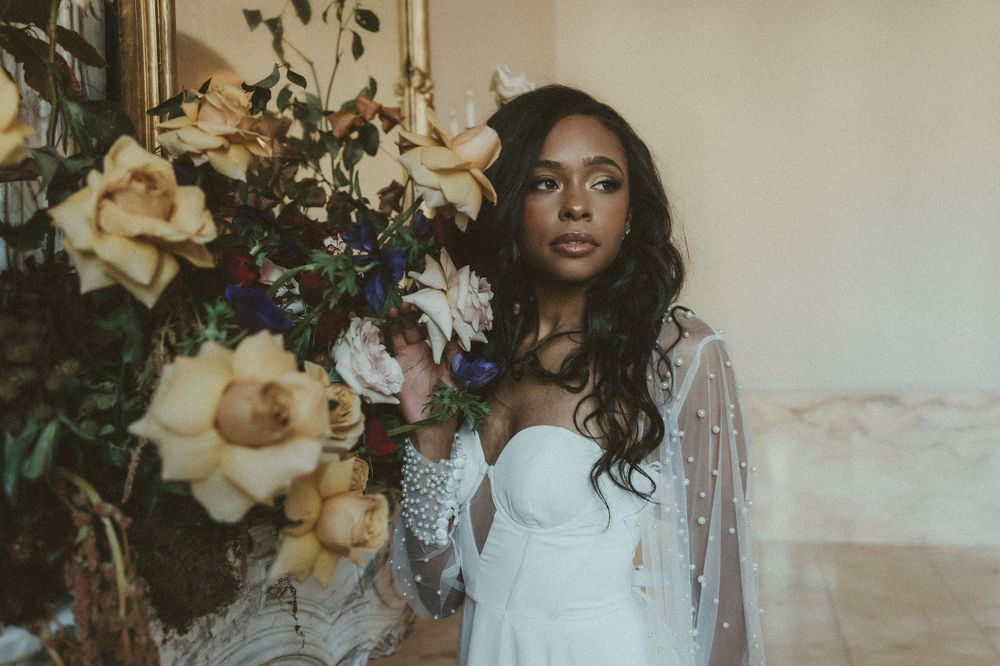 Ethereal bridal portrait with flowing dress beside elegant floral arrangement.