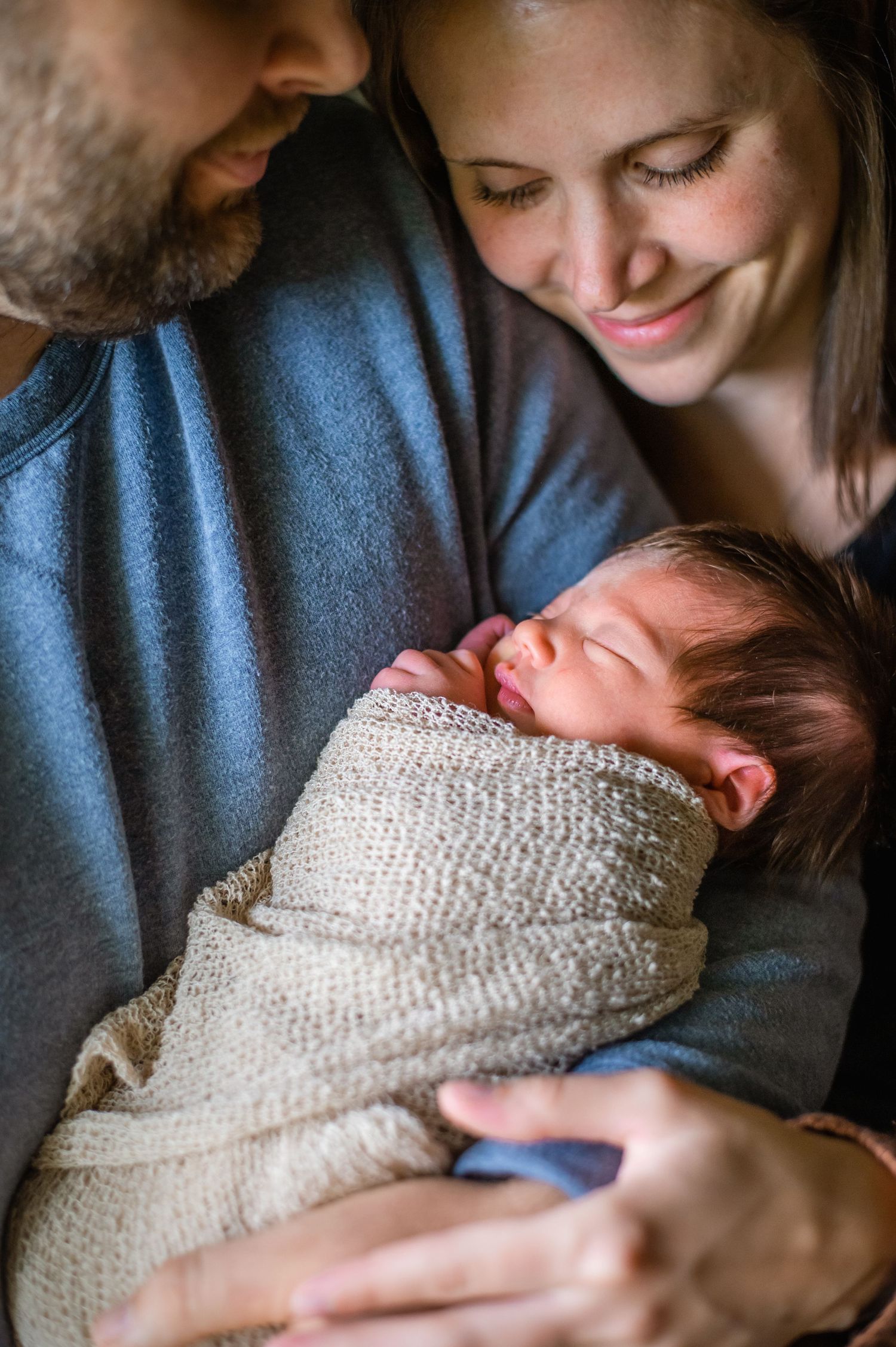 An intimate indoor family portrait captures a tender moment in soft lighting.