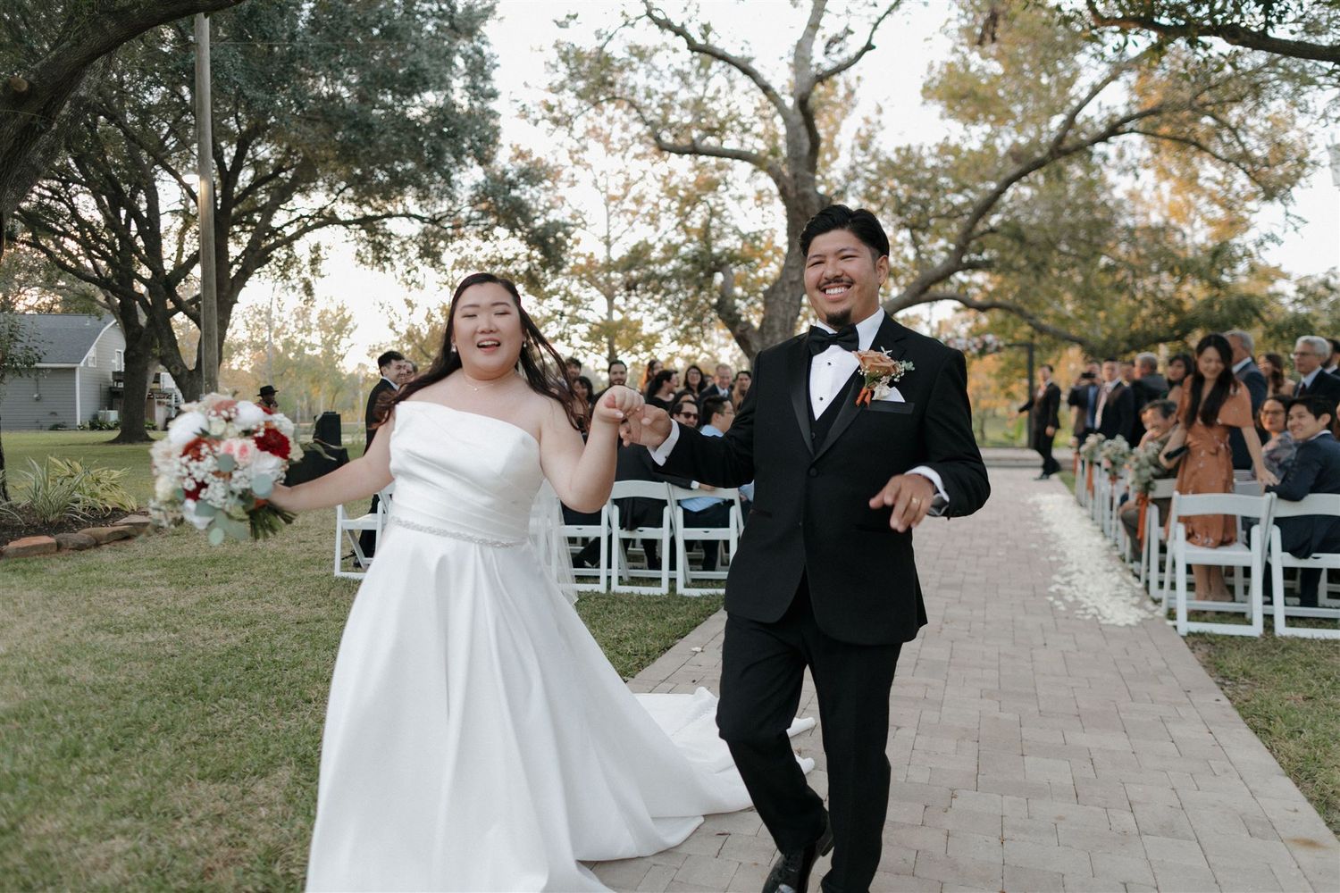 Joyful wedding couple celebrates while walking down stone pathway after ceremony.