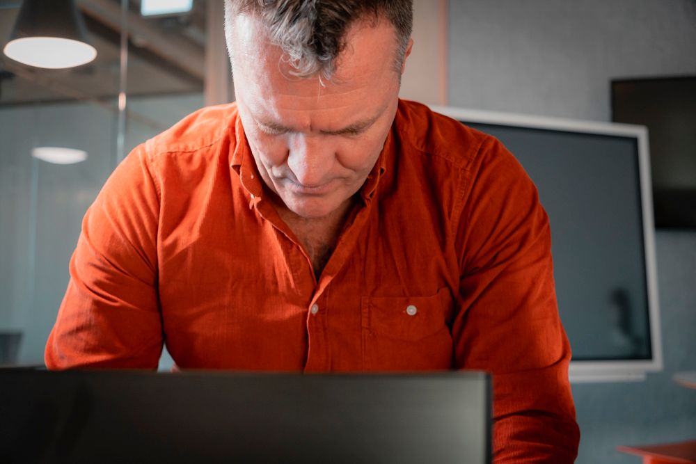 ceo man with red shirt looking down at laptop