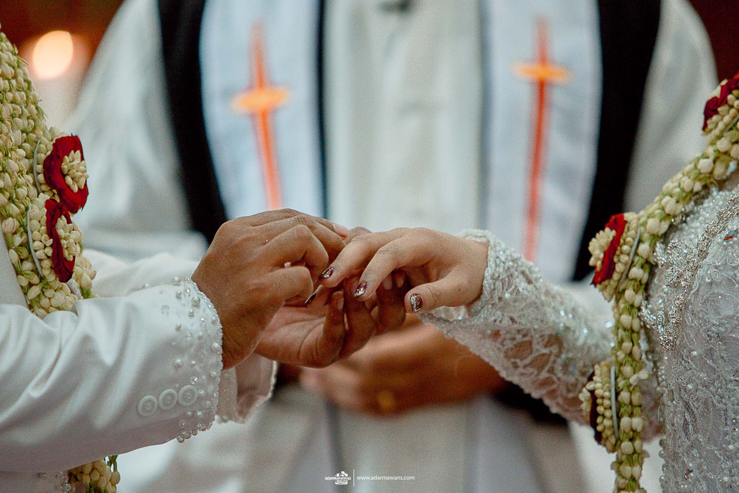Close-up of hands exchanging rings during Christian wedding ceremony with priest's robe visible.