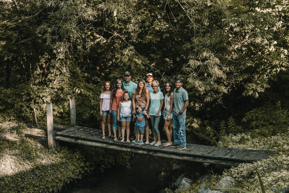 A group posing together on a wooden footbridge in a wooded setting.