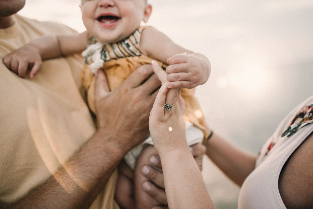 Hands holding a small baby wearing a yellow striped outfit in soft lighting.