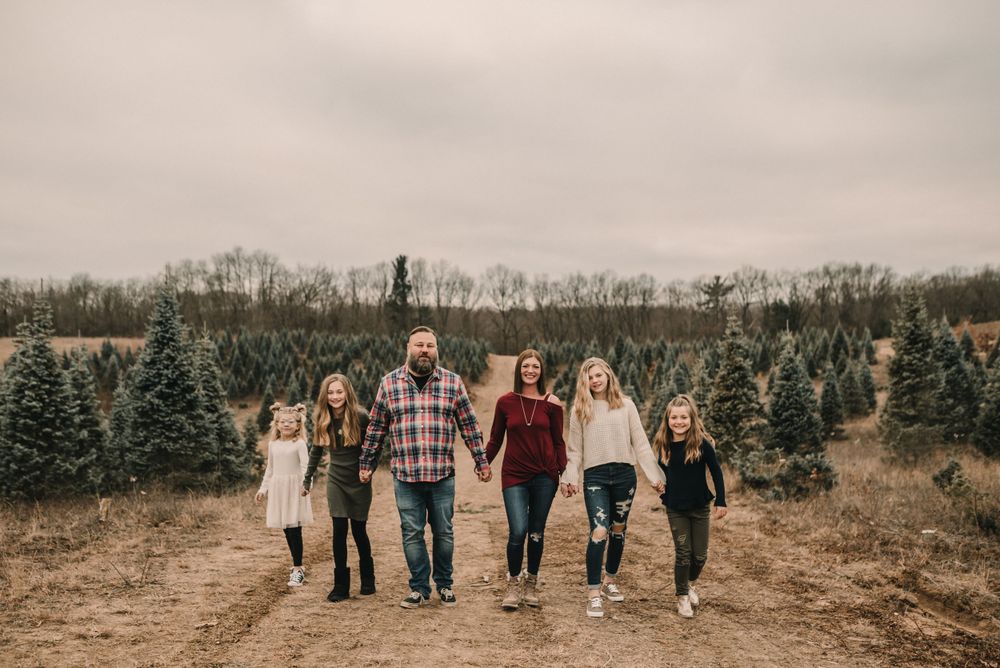 Family walking hand in hand through a Christmas tree farm on an overcast day.