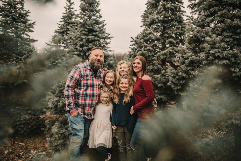 A cheerful group poses together among evergreen trees with atmospheric smoke effects.