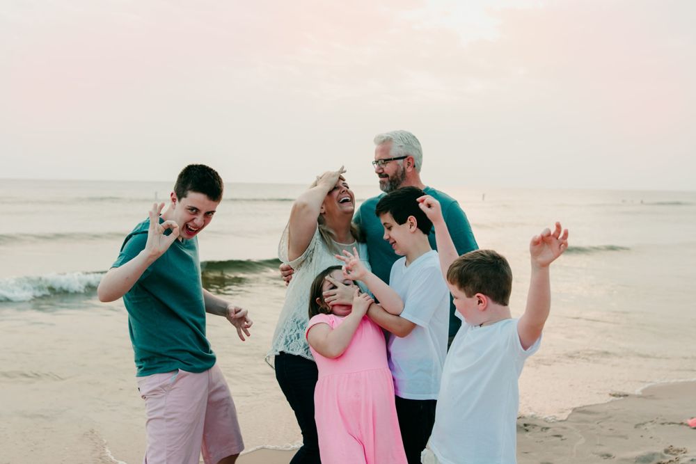 A joyful group poses playfully together on a beach at sunset.