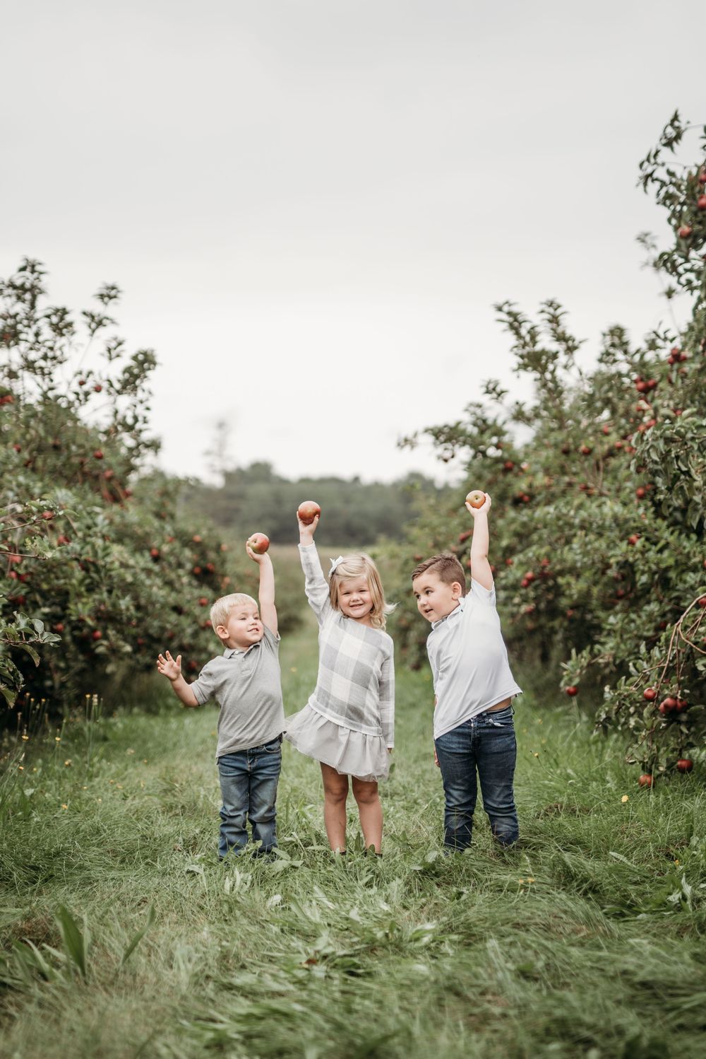 Three children holding apples up in celebration at an apple orchard.
