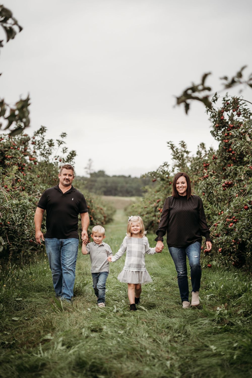 A family walking together through rows of apple trees in an orchard.