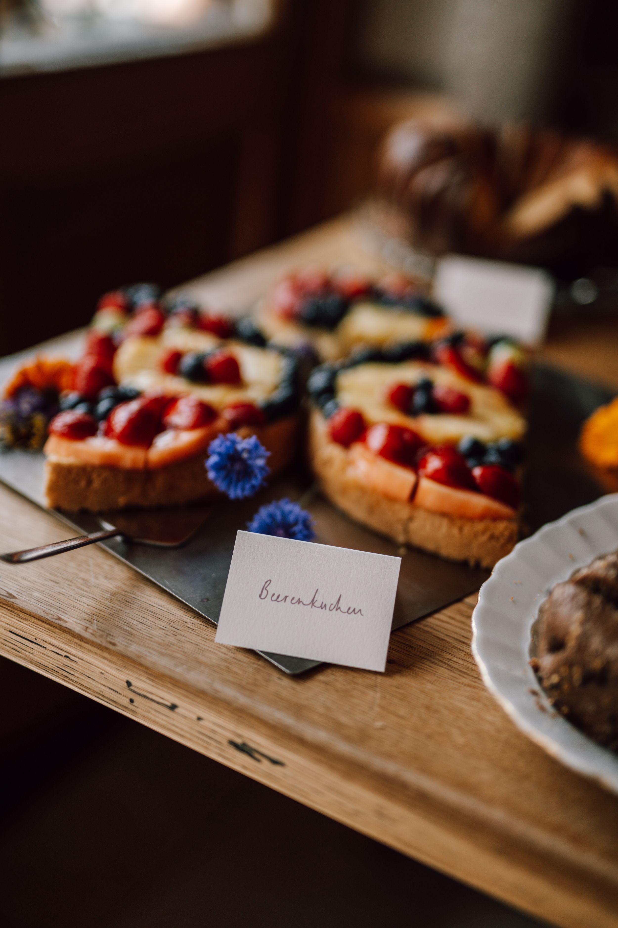 Fresh berry tarts with blue flowers and name card displayed on rustic wooden surface.