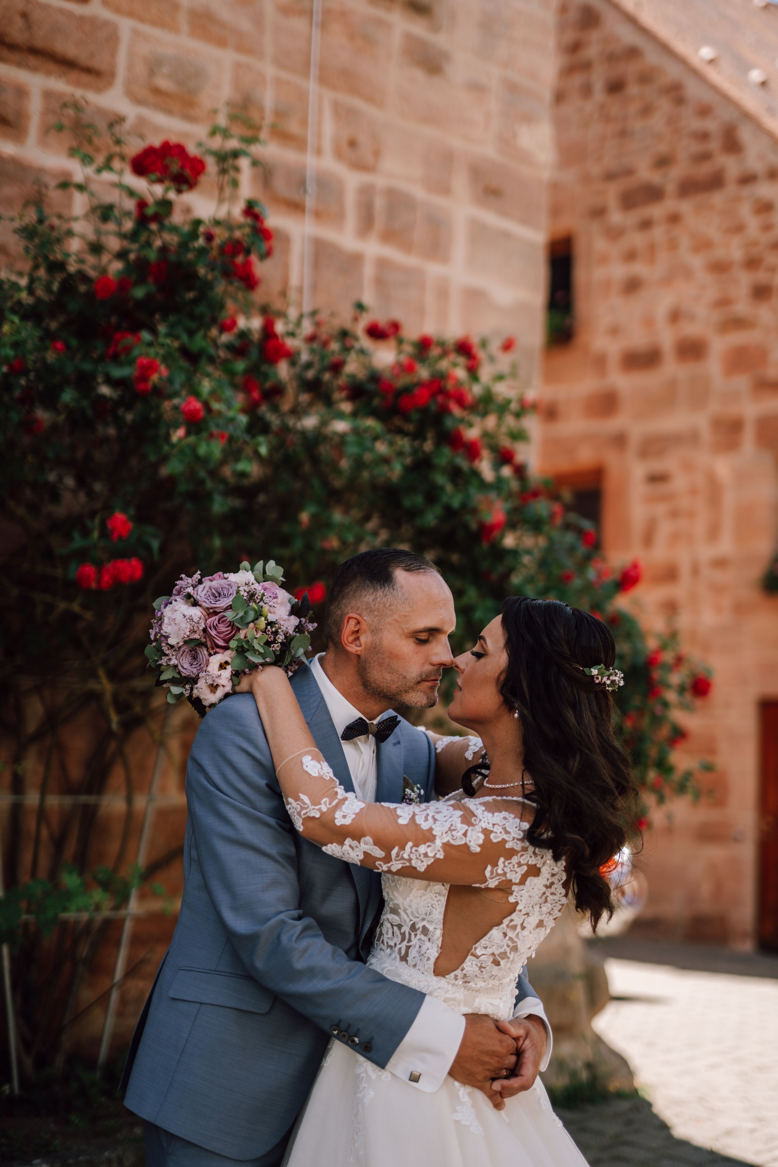 Romantic wedding couple embracing against stone wall with red roses.