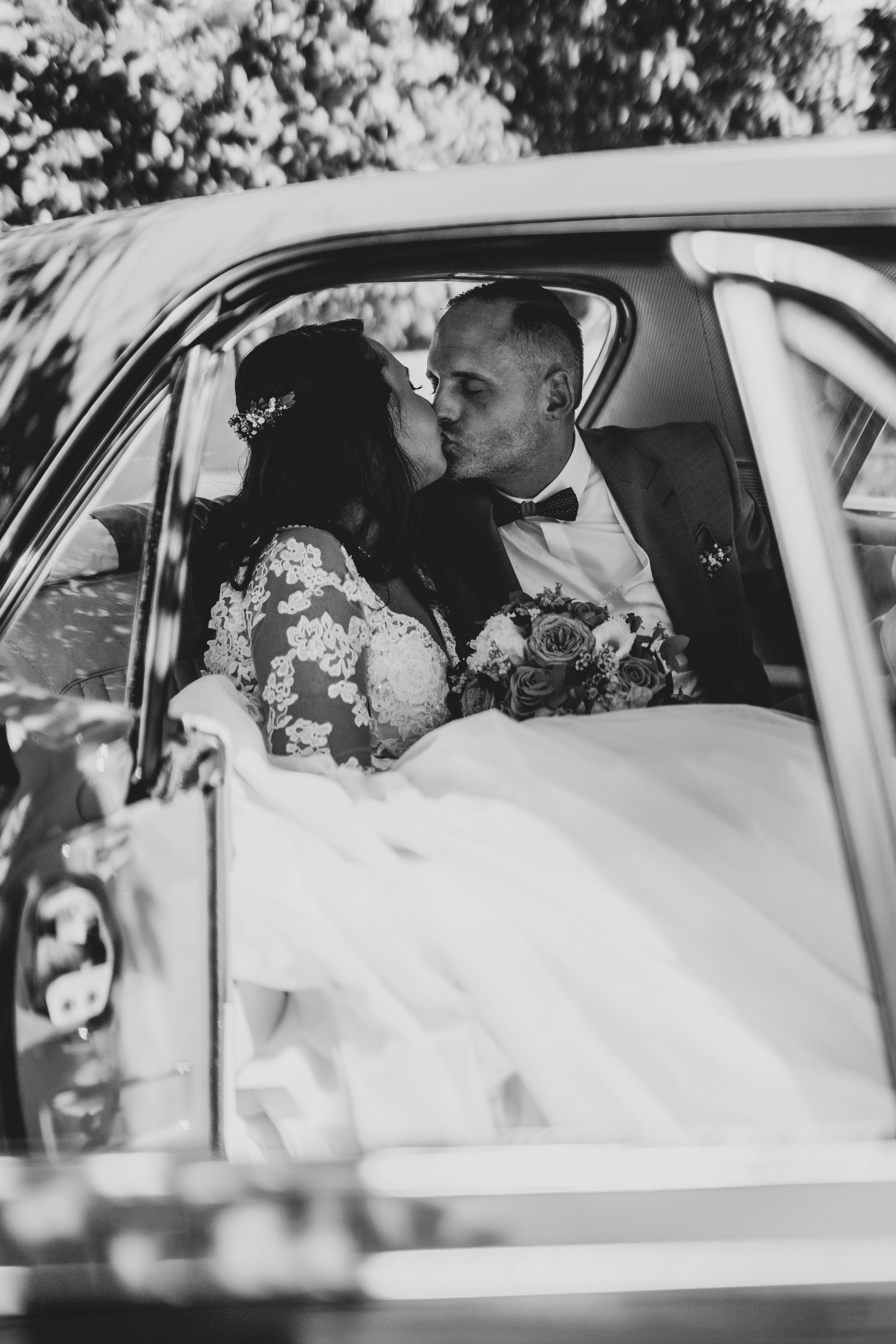 Black and white photo of newlyweds sitting in vintage car after ceremony.