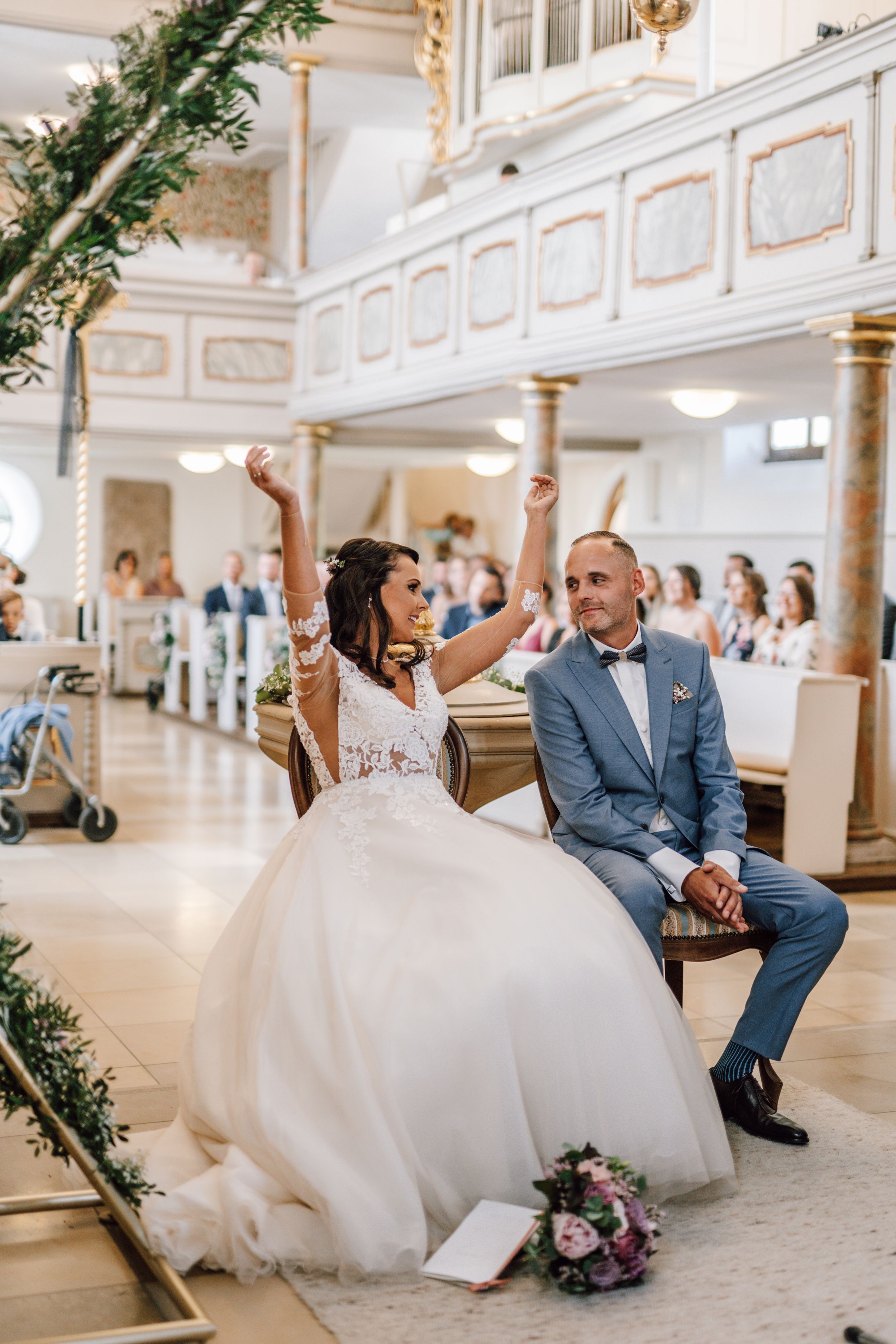 Bride in white gown sitting on ornate floor during wedding reception.