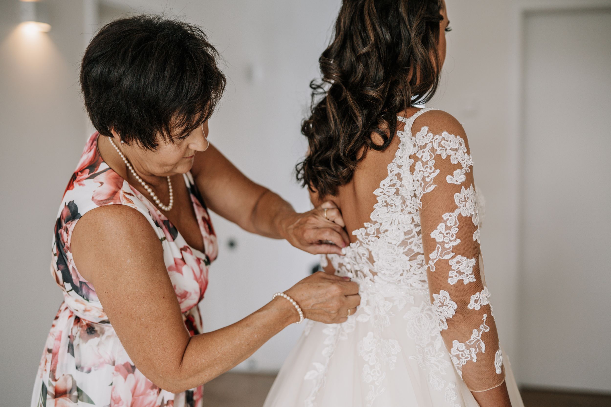 Hands carefully fastening buttons on the back of a white lace wedding gown.
