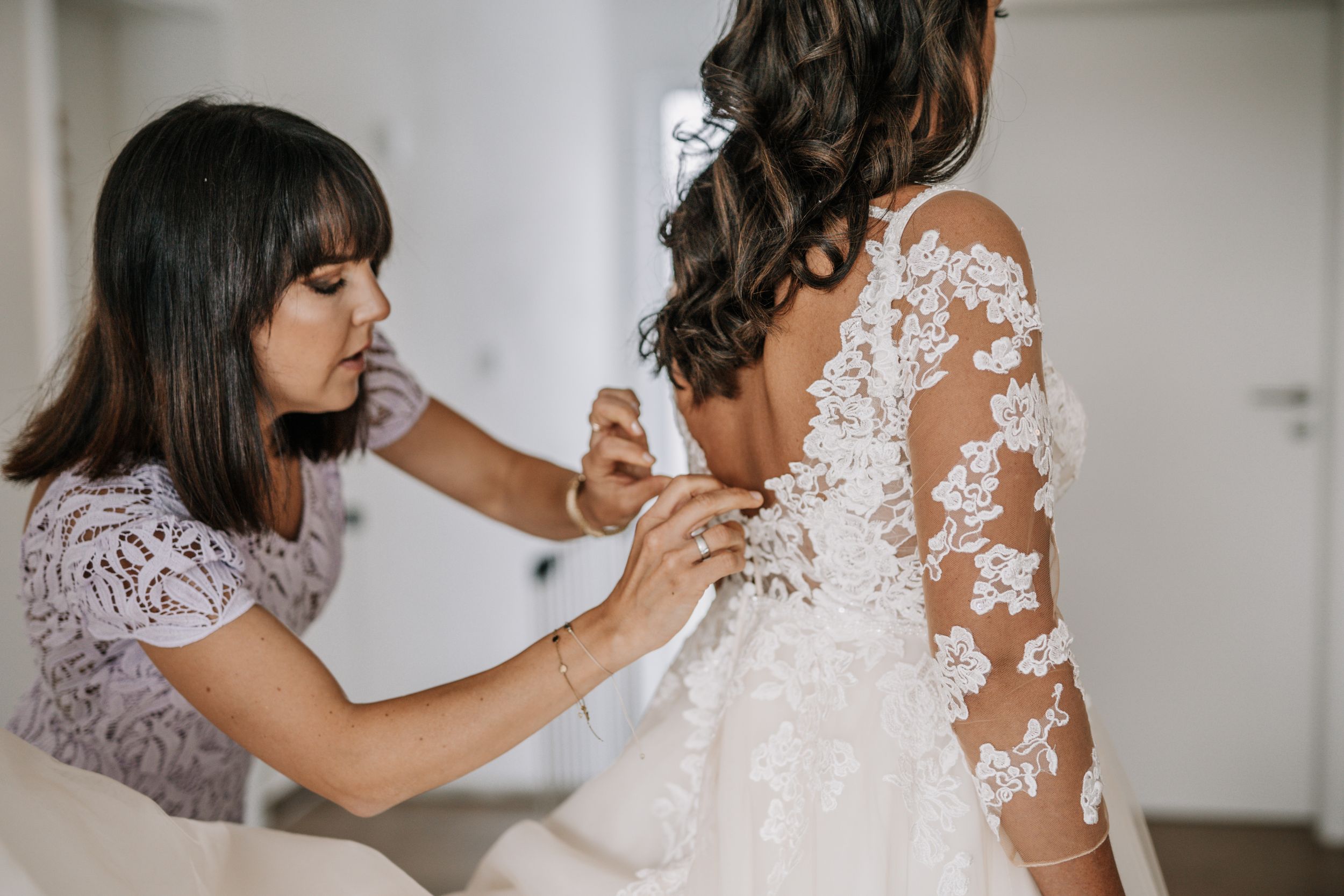 Close up of hands adjusting delicate lace details on a wedding dress.
