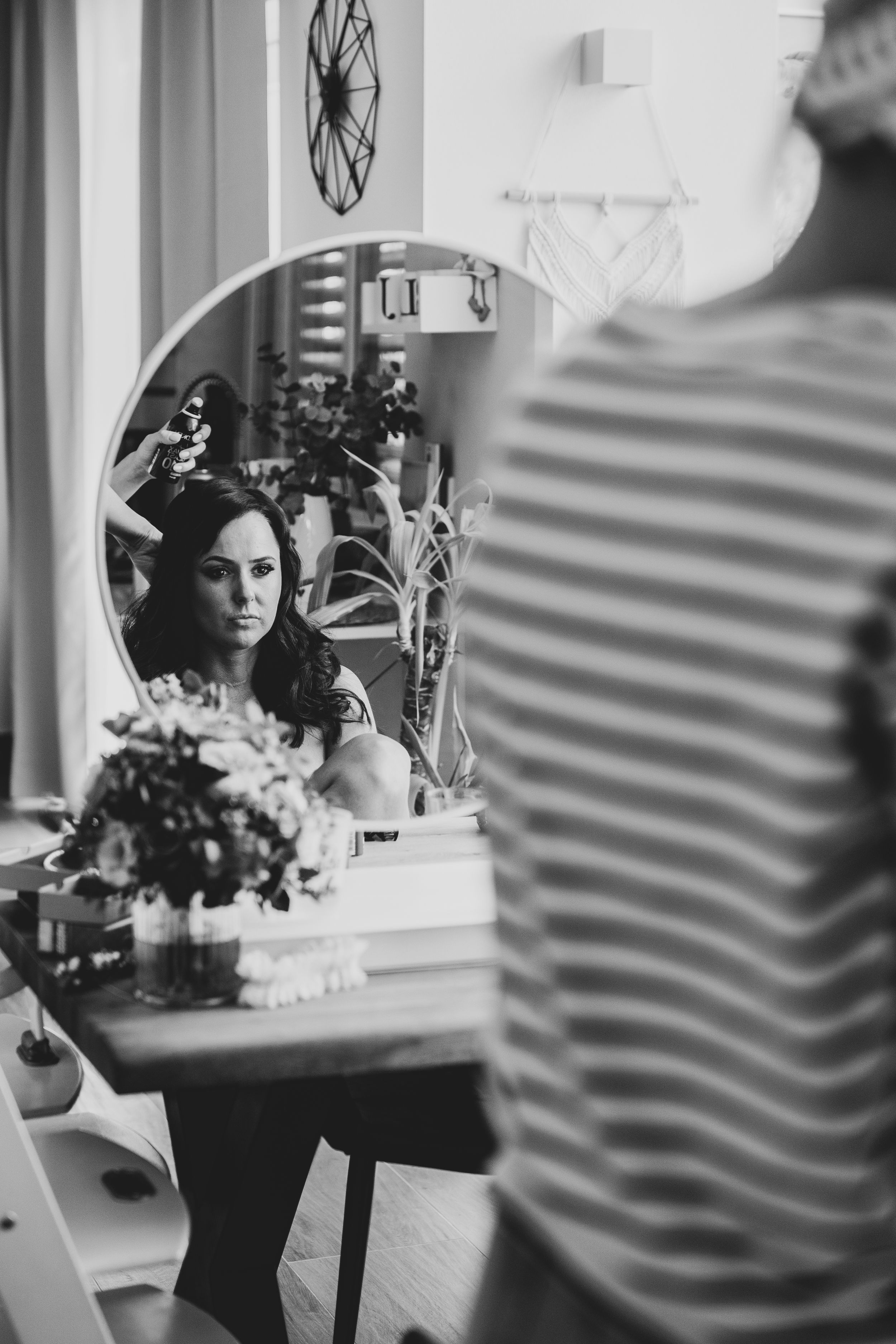 Black and white reflection of a bride getting ready in a salon mirror.