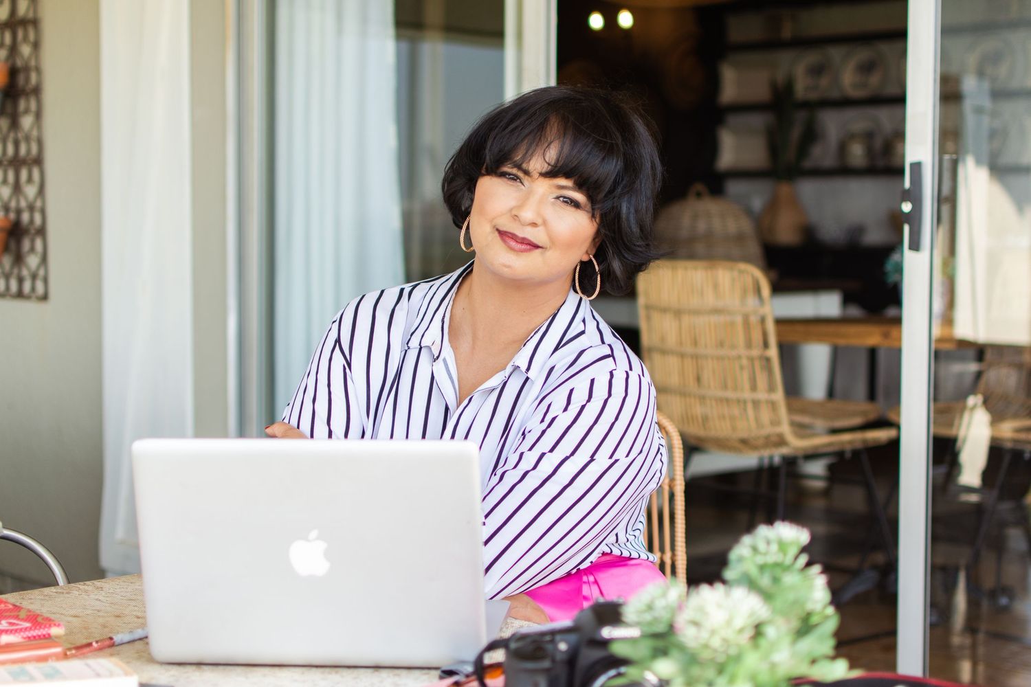 Person in striped shirt working on MacBook laptop with plants on desk.