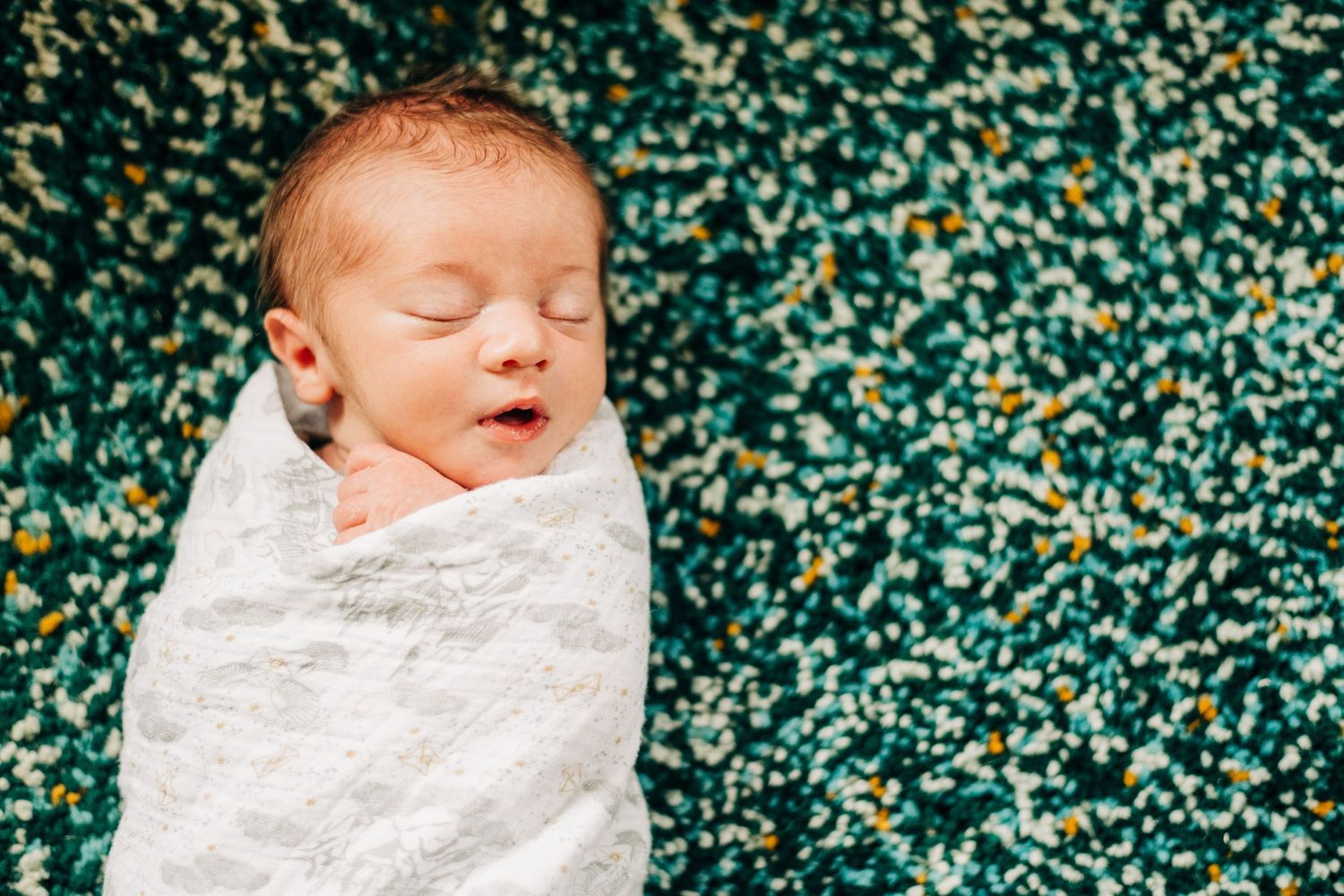 baby laying on a blue rug wrapped in a white blanket