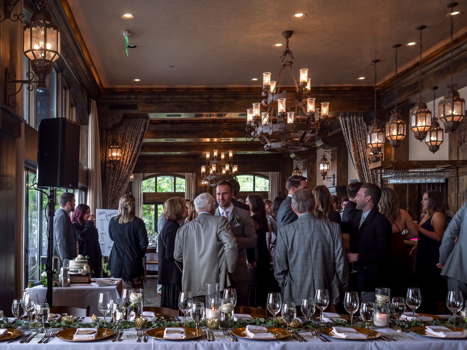 Elegant dining room with wooden beams and chandeliers hosts a formal gathering of guests during an evening event.
