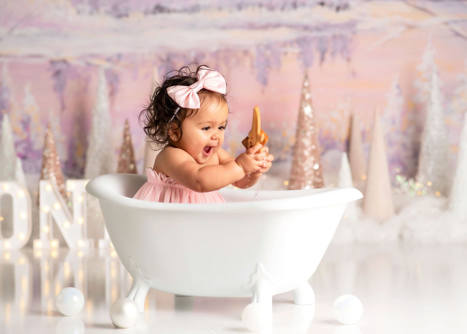a baby laughs while holding a wooden toy in a tiny bathtub