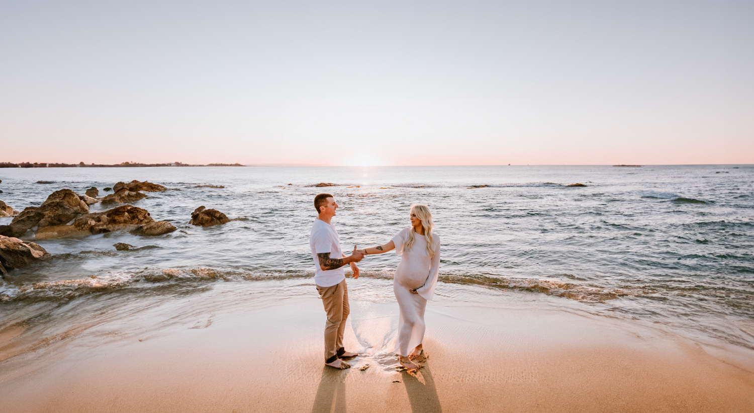 Couple walking along a rocky beach shoreline during sunset.