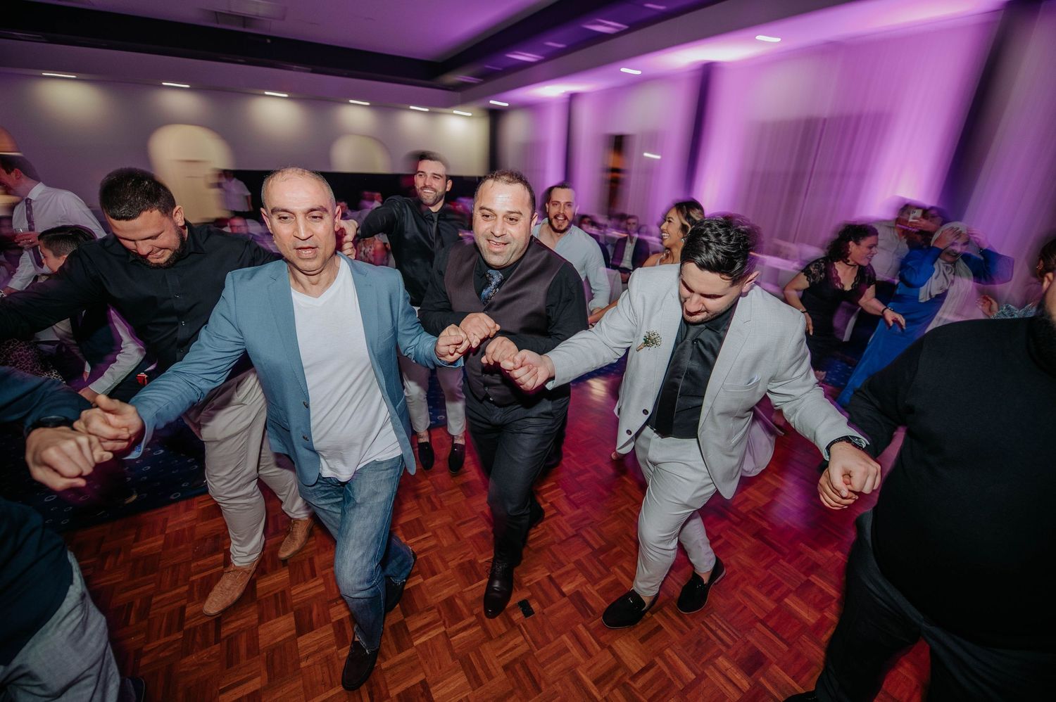 Group of energetic wedding guests dancing on red carpeted floor at reception.