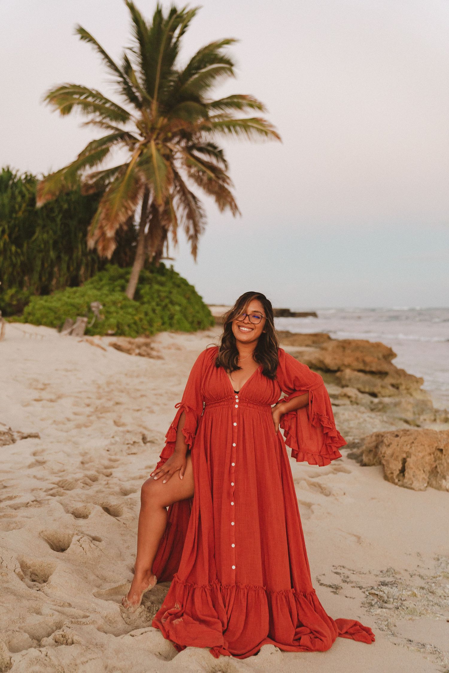 Photographer Kelly Pagan of Moments With Kell posing on the beach with her burnt orange dress on Oahu in Hawaii