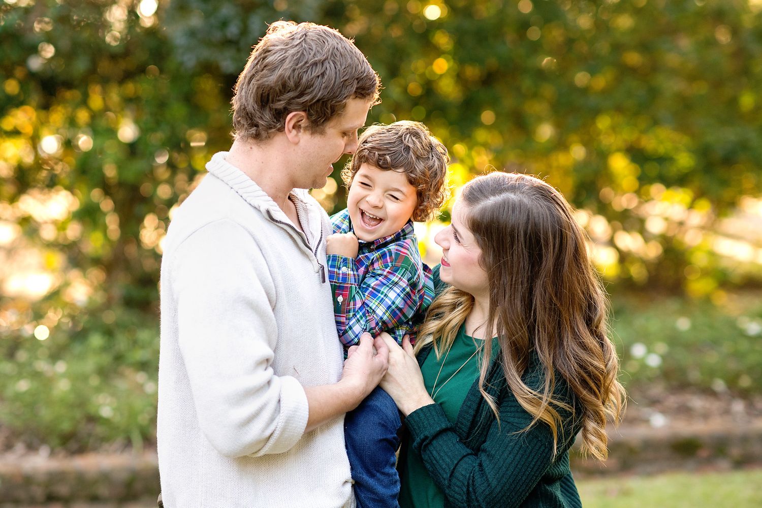 A happy family of three enjoys a playful moment together in a lush autumn park setting.