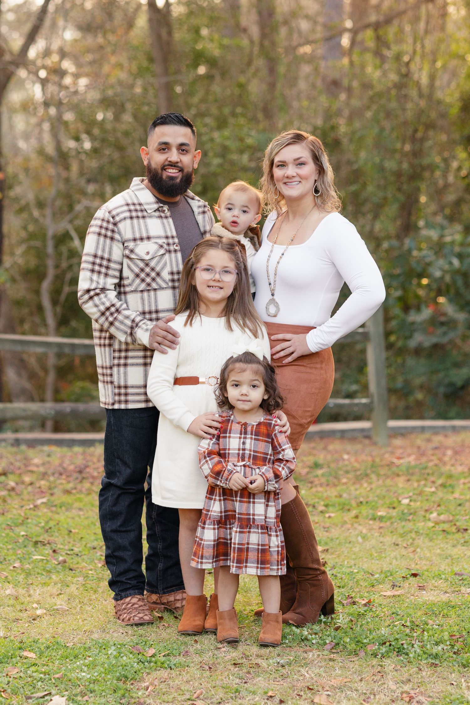 Family stands together for a portrait wearing coordinated outfits in plaid and white.
