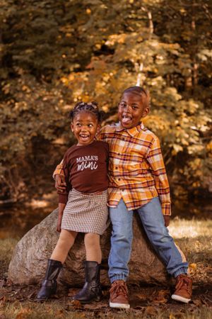 Children sitting and laughing together on rocks in an autumn forest setting.