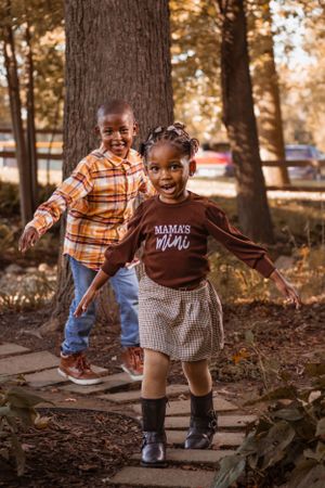 Two young children playing and running on a wooden path amid fall foliage.