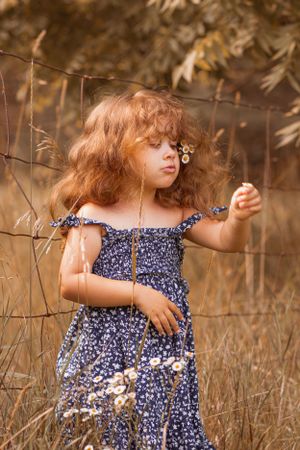 Child in navy dress explores rustic fence line surrounded by dried grass.
