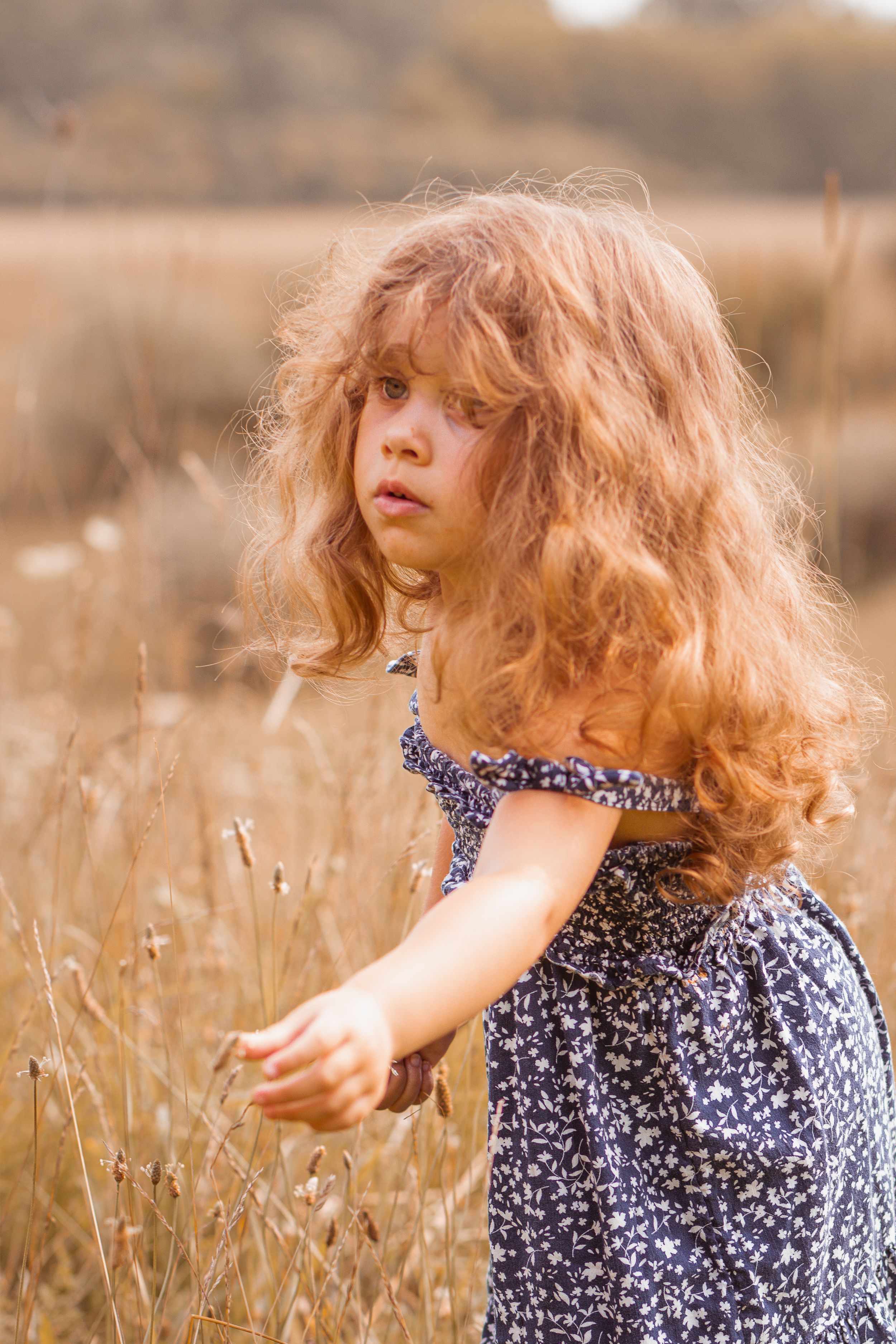 Child with flowing hair gazes thoughtfully in summer field.