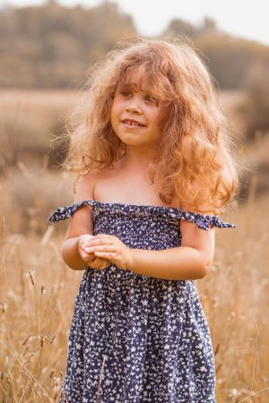 Child in off-shoulder dress poses cheerfully in sunny meadow.