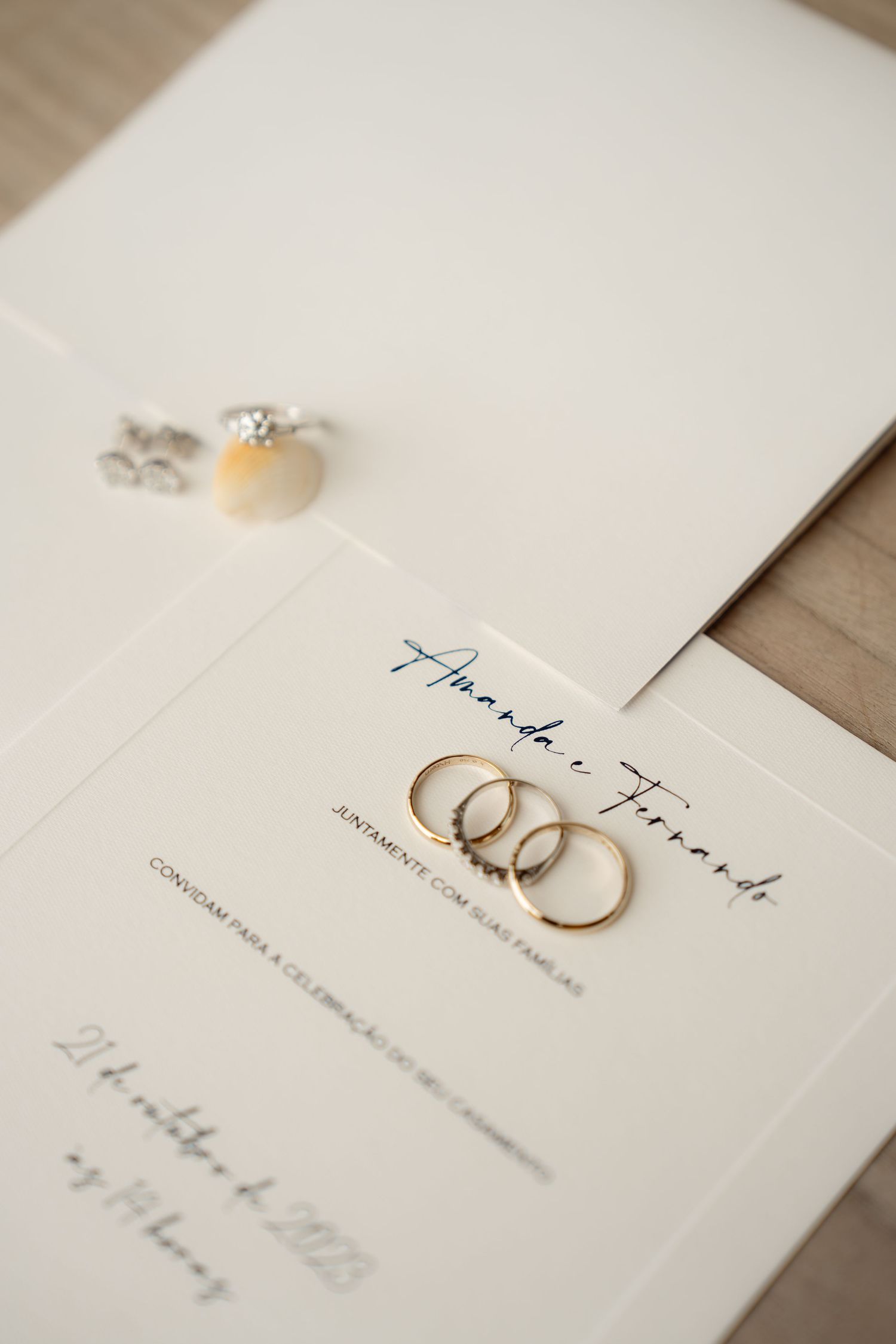 Wedding rings and invitation cards laid out on a light wooden surface.