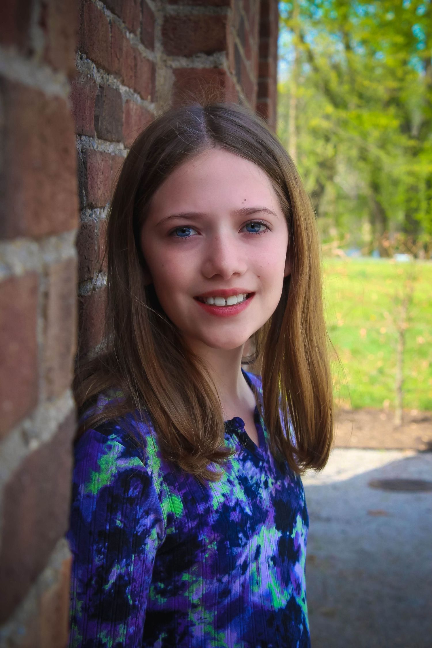 A portrait against a brick wall wearing a blue tie-dye patterned dress.
