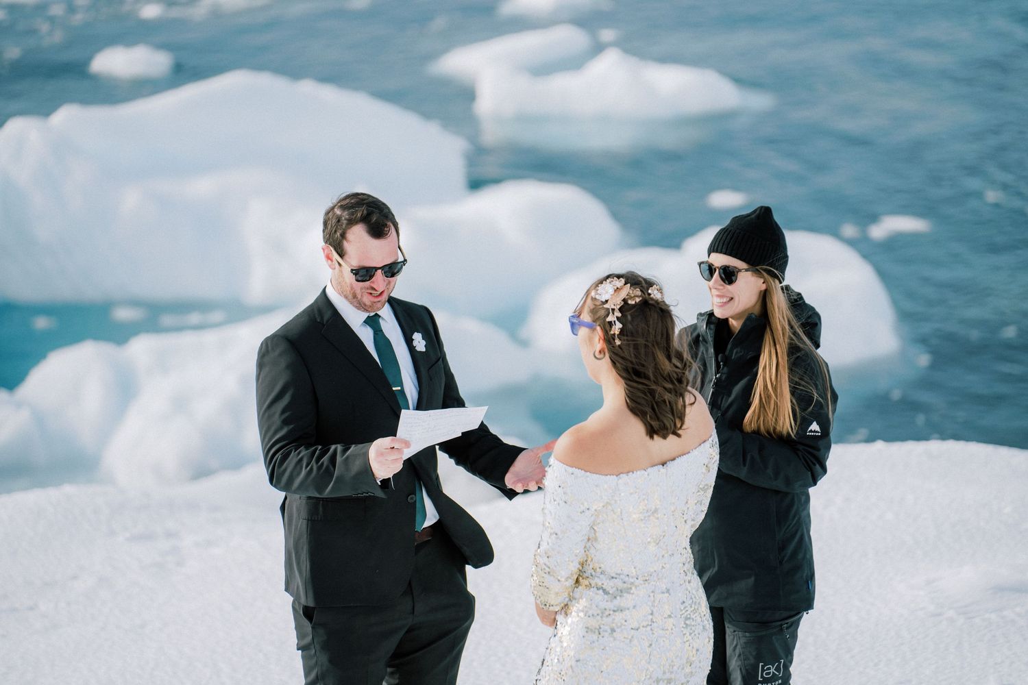 Wedding ceremony being conducted on snow-covered terrain with icebergs floating behind.