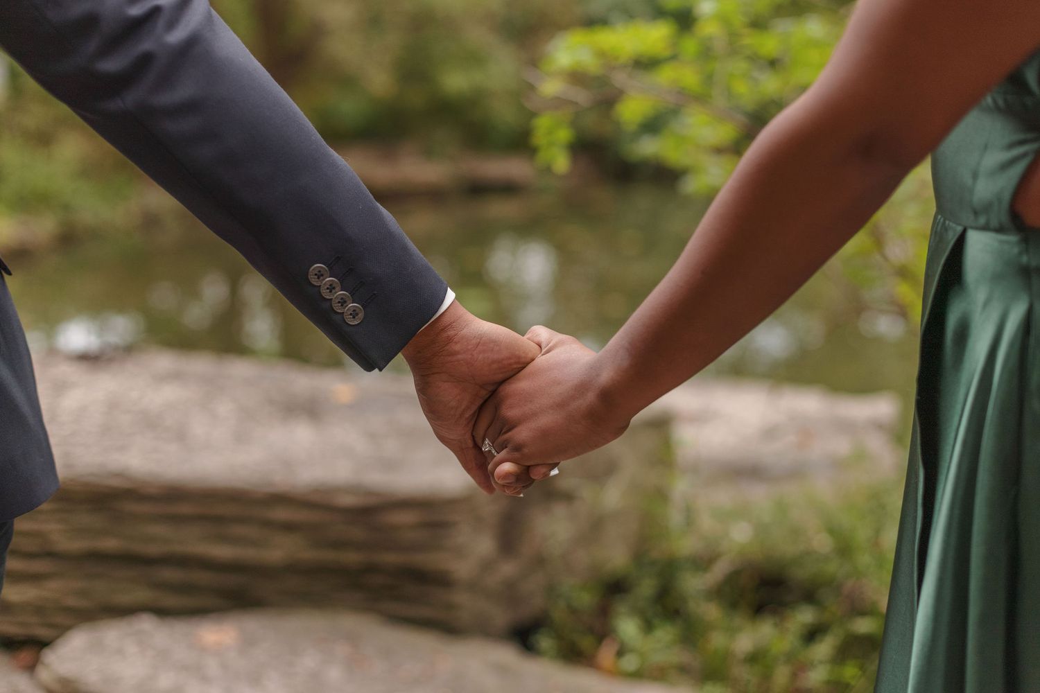 Close-up of a couple holding hands against a natural outdoor background with water feature.
