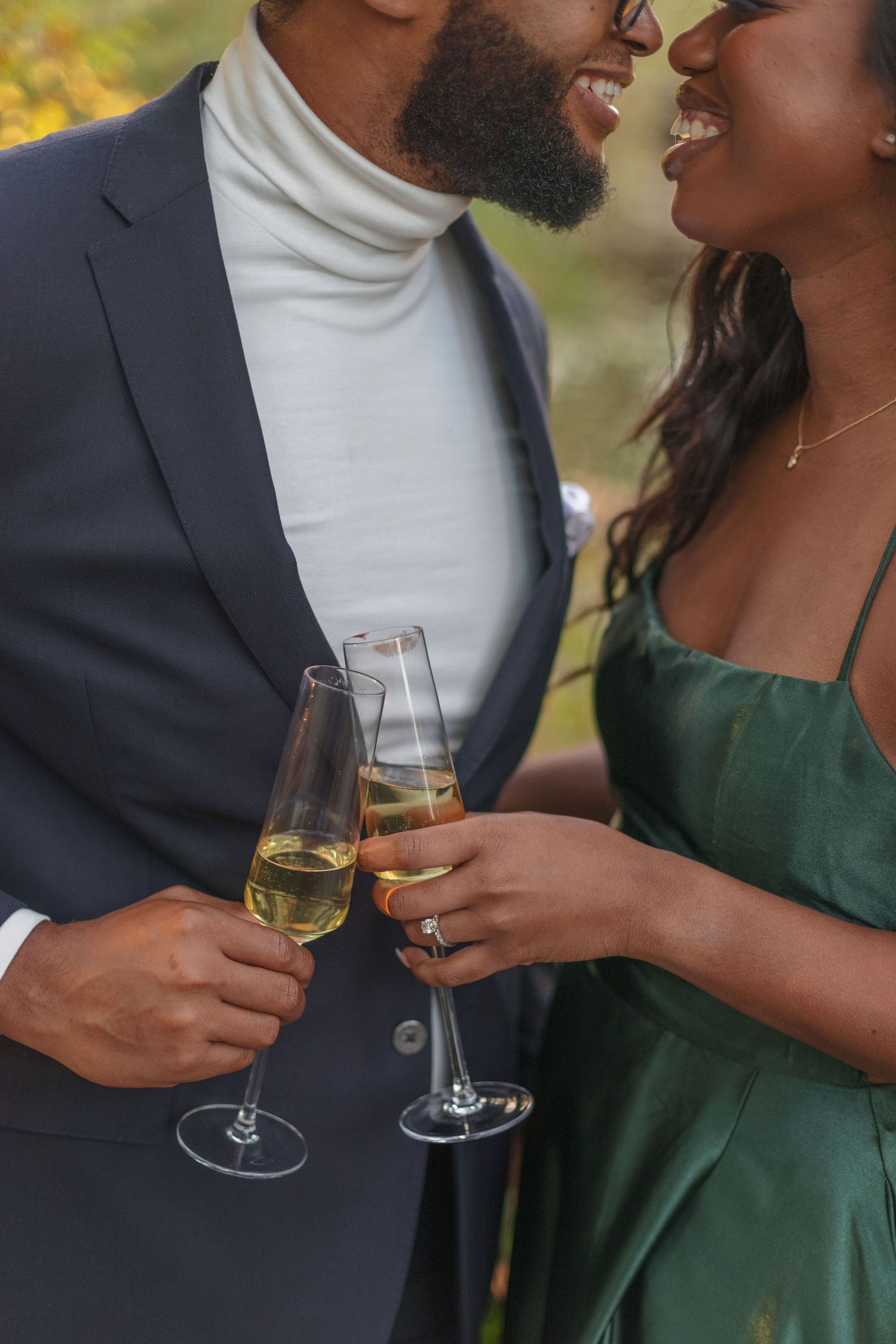 A couple shares a close intimate moment while toasting with champagne glasses outdoors.
