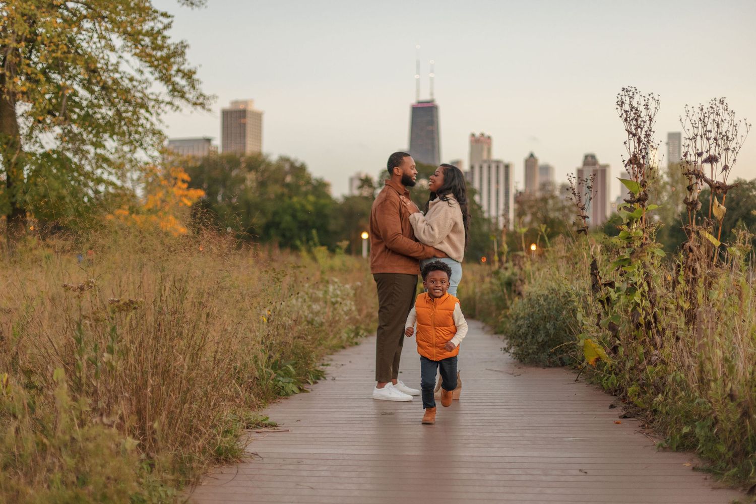 A family walks together on a boardwalk path with Chicago skyline visible in the distance.