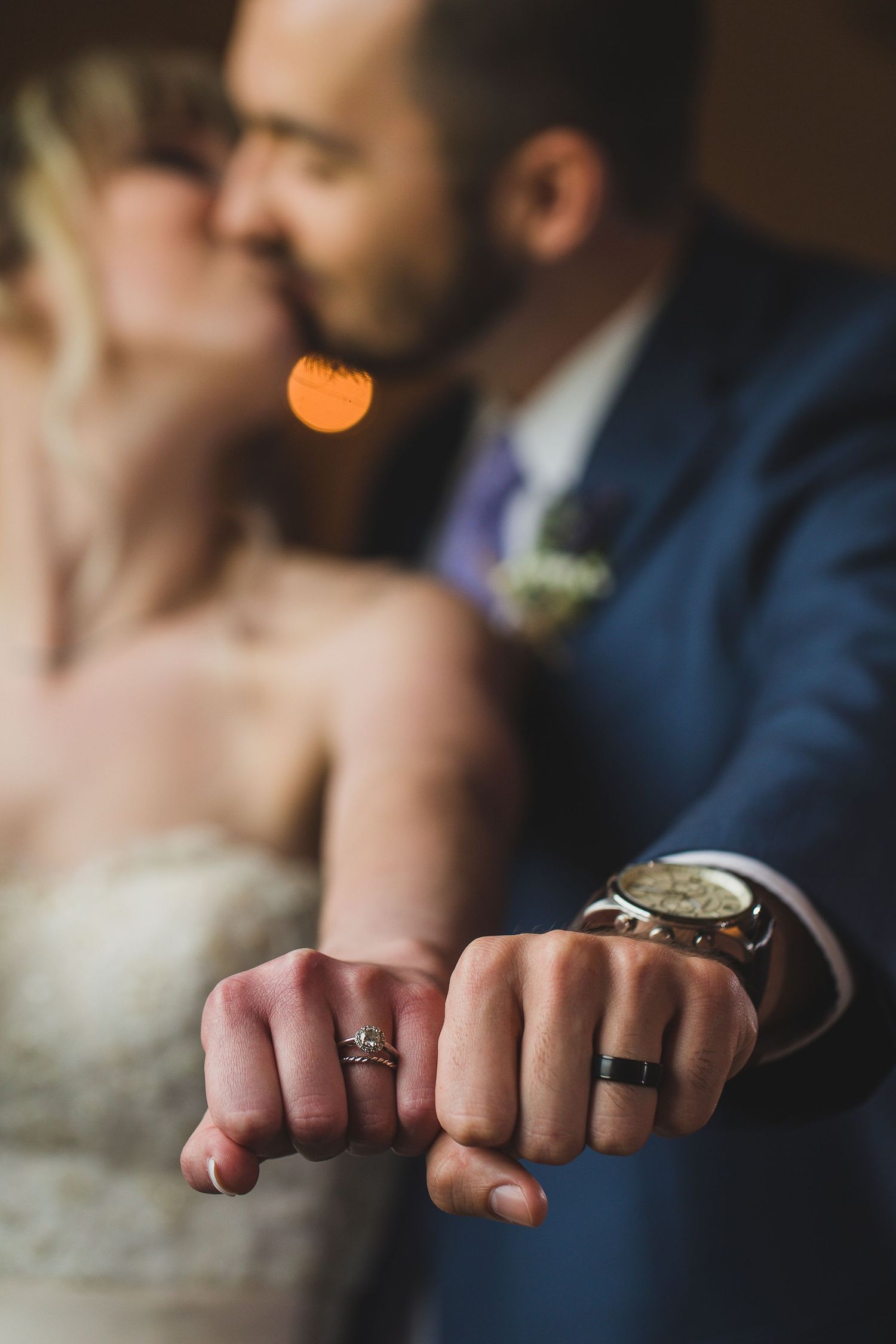 Close-up of wedding rings on hands against dark background.