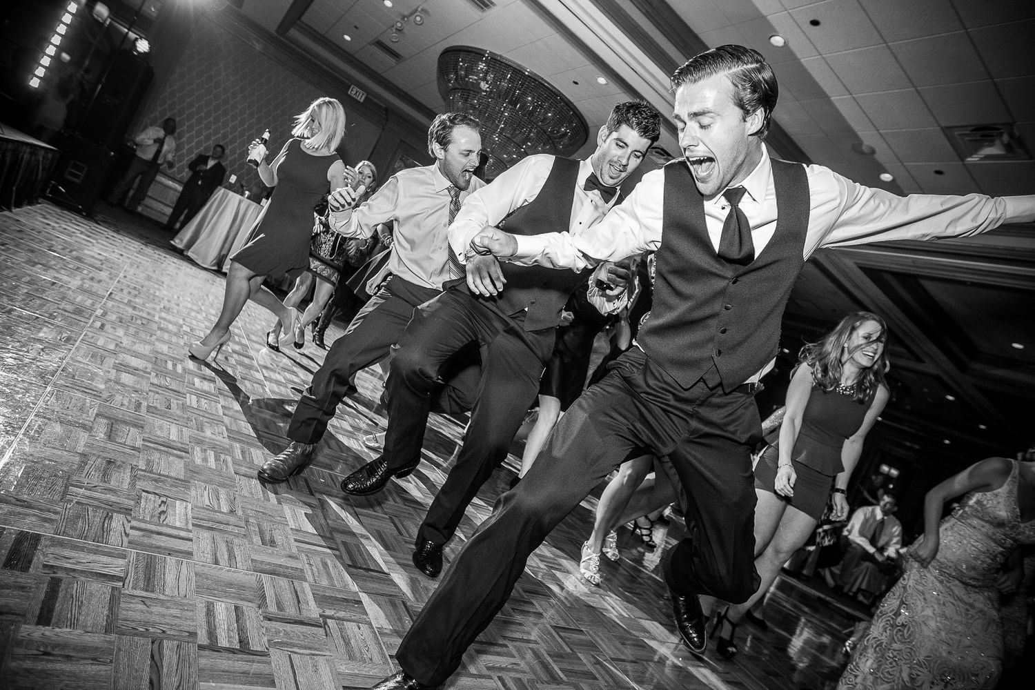 Black and white photos of wedding guests dancing and celebrating on a patterned dance floor.