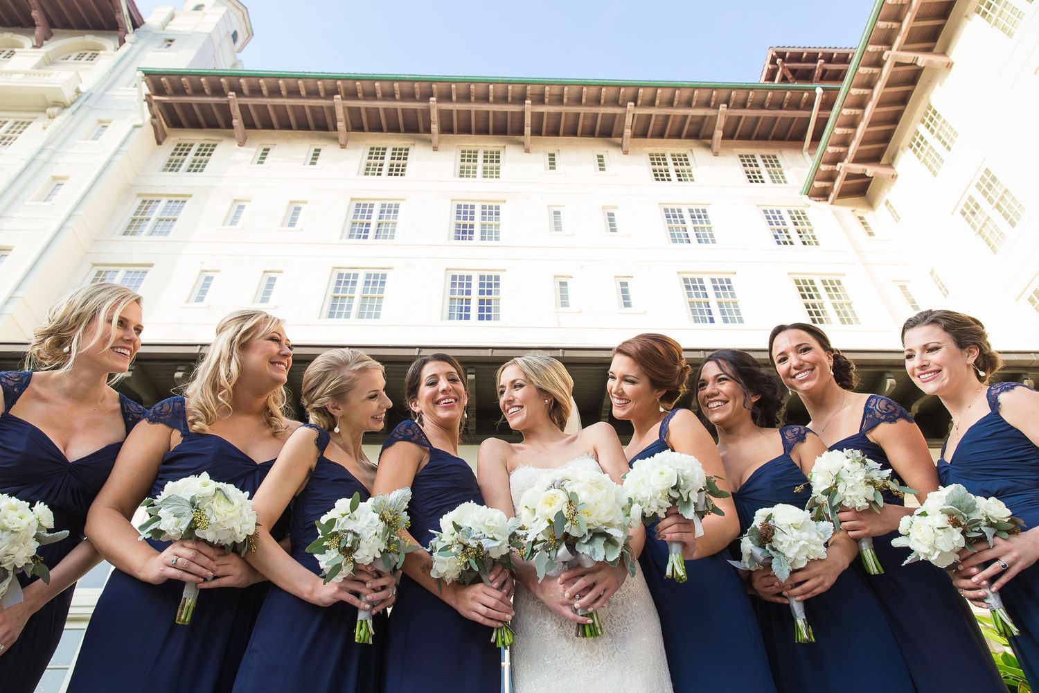 Wedding party members in navy and white holding bouquets while posing outdoors.