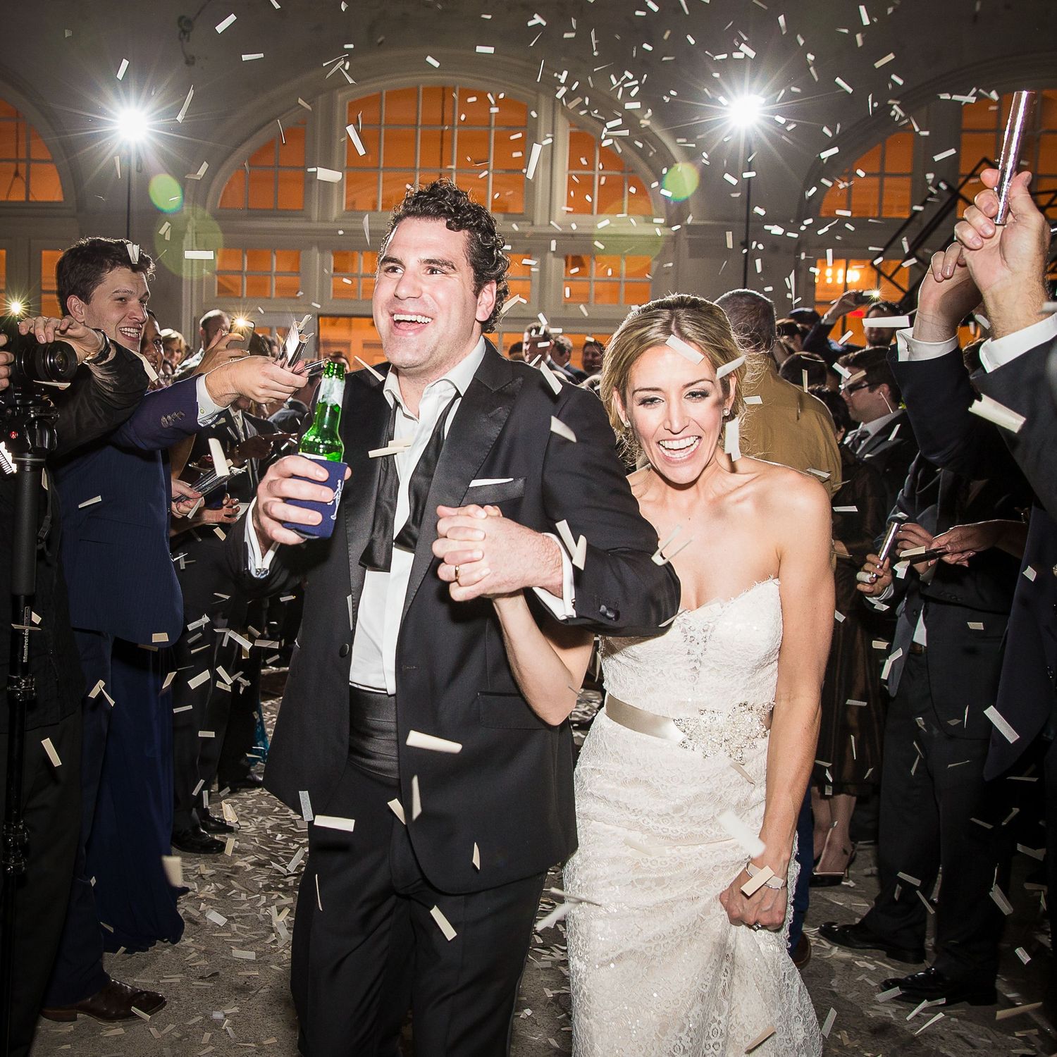 Newlyweds walking through confetti shower during evening wedding celebration.