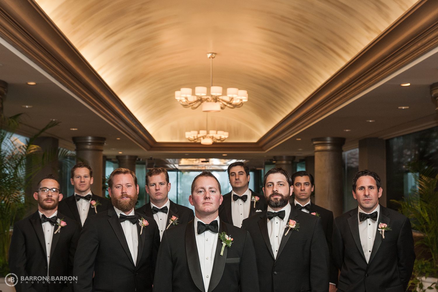 Groomsmen in black tuxedos and bow ties lined up for formal wedding photo.