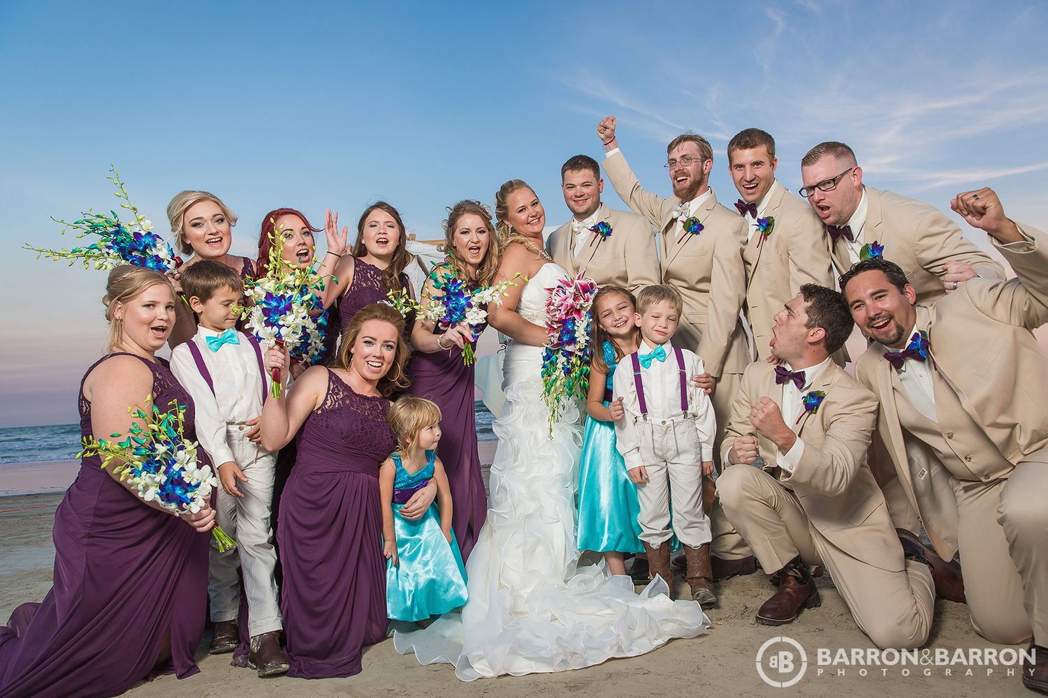 Wedding party celebrating on a sunny beach with turquoise water and sand in the background.