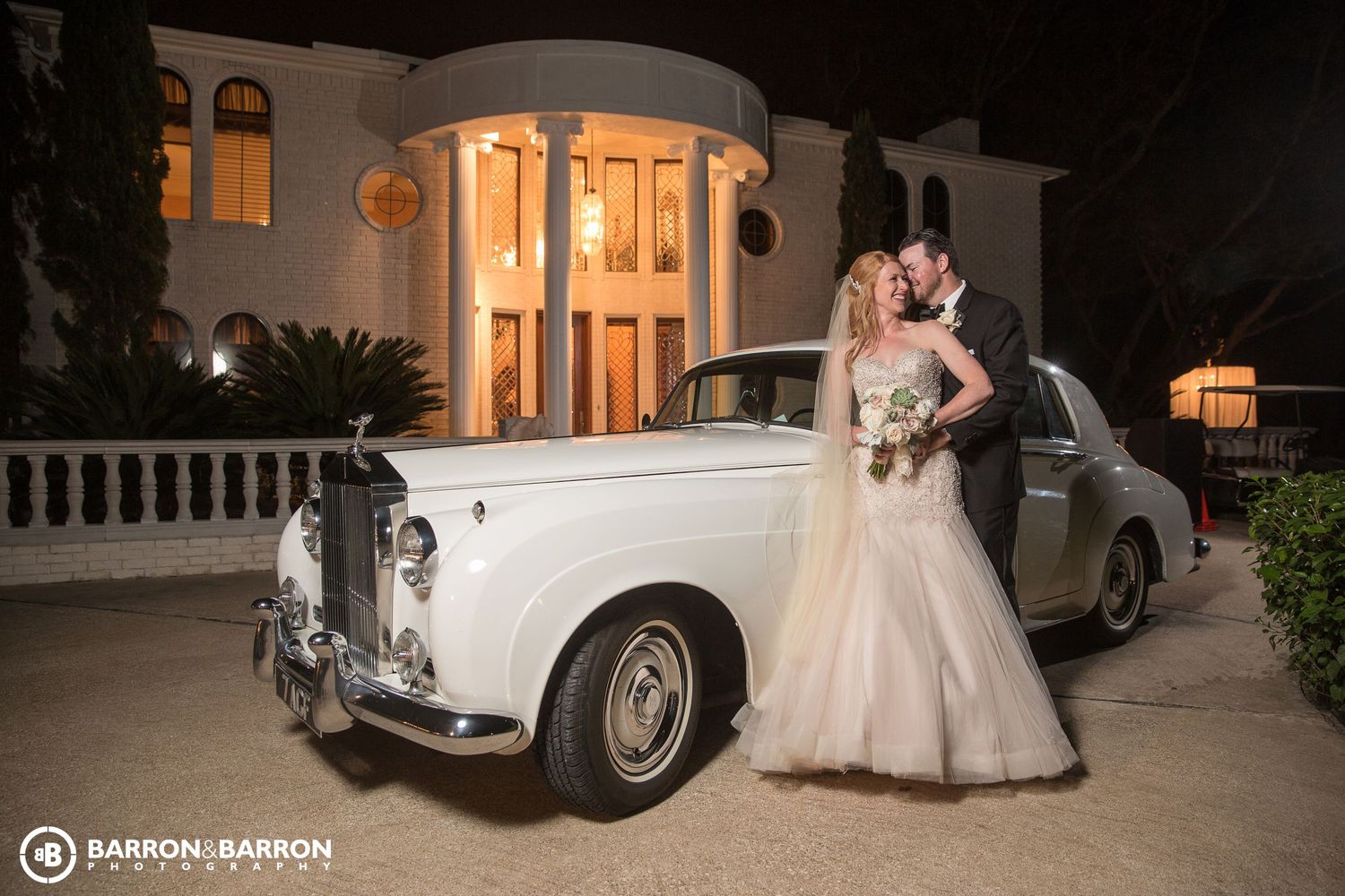 Classic white Rolls Royce parked outside an elegant venue at night.